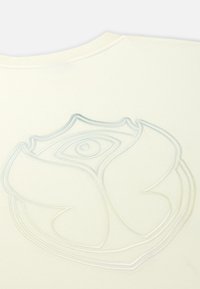 Crème-kleurig t-shirt met een textuur, tonale reliëf logo-ontwerp dat lijkt op een bloem en een oog. Zachte stof met een ronde hals.