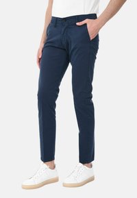 Chinos blu navy in cotone, design slim fit con tasche anteriori e chiusura con bottone visibile; abbinati a sneakers bianche.