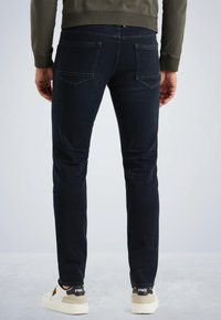 Jean slim fit bleu foncé en denim, avec deux poches arrière et une taille mi-haute, associés à des baskets blanches.
