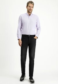 Camicia button-up di un leggero lavanda con maniche lunghe, abbinata a jeans neri. L'outfit è completato da scarpe da ginnastica grigie.