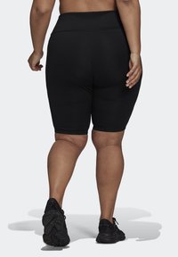 Black high-waisted bike shorts with a smooth texture, fitted design, and mid-thigh length, paired with black athletic shoes.