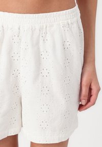 Hvite bomullsshorts med øyelets mønster, med elastisk midje og blomsterbroderidetaljer. Myk tekstur, avslappet passform.