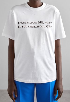 Wit katoenen T-shirt met korte mouwen, voorzien van zwarte bedrukte tekst: "genoeg over MIJ, wat vind jij van MIJ?" aan de voorkant.