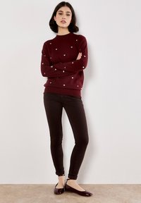 Pull bourgogne avec de petits motifs en forme de cœur argenté, assorti à un jean sombre et des ballerines bourgogne brillantes, présentant un col rond et un ourlet côtelé.