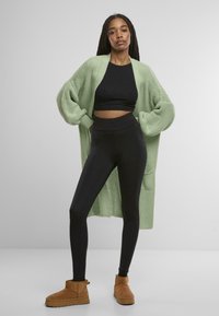 Lång, oversized cardigan i ljusgrön stickning, ihop med en svart crop top och högmidjade leggings. Bruna mocka ankelskor.