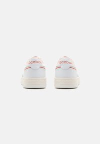 Valged madalad Reeboki sneakerid roosa aktsentidega, kujutatud seljaga tavalise helesinise tausta ees.