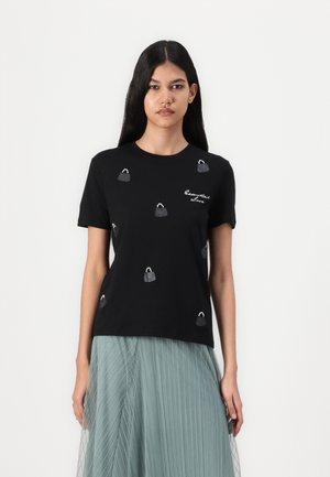 T-shirt en coton noir à manches courtes, avec des motifs de sacs à main brodés en gris et blanc, associé à une jupe plissée bleu clair.