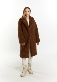 Brun fluffy oversized frakke med kilekrave, to frontlommer og en afslappet silhuet, parret med lysebeige combat støvler.
