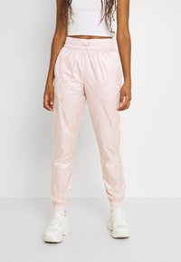 Ljusrosa, glansiga joggingsbyxor med elastisk midja, slim fit och smalnande mudd; bärs tillsammans med en vit crop top och vita sneakers.