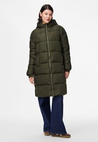 Casaco tipo puffer verde-oliva com capuz, apresentando um fecho de correr frontal completo, um tecido texturizado e dois bolsos laterais. Usado sobre umas calças de ganga largas azul-escuro.