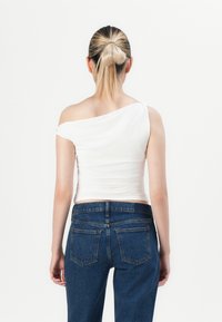 Hvit off-shoulder topp med rynkedesign og glatt tekstur. Kombinert med mørkeblå denimjeans med standard baklommer og rett ben.