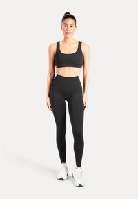 Schwarzer Sport-BH und hoch taillierte Leggings aus glattem, dehnbarem Stoff, mit einer Seitentasche und einem eng anliegenden Design.
