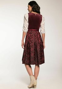 Bordeauxrotes Kleid mit einem Samtoberteil und einem blumenmusternden Rock, der gepuffte Spitzenschultern und eine taillierte Taille hat. Beigefarbene Knöchelstiefel runden den Look ab.