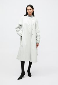 Világosszürke ballonkabát gombos elülső résszel, hosszú ujjakkal és laza szabással. Válldíszítésekkel rendelkezik, és középhosszban ér, hogy fedettséget biztosítson.