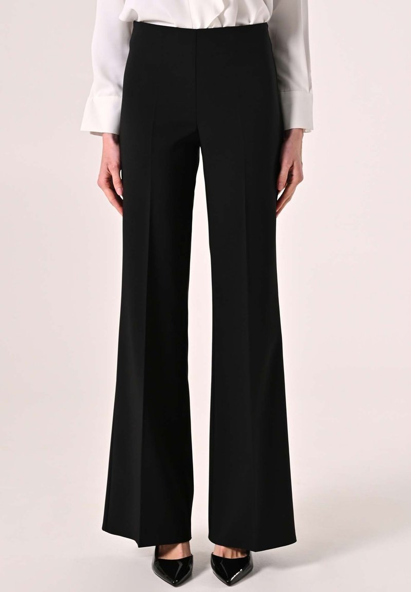 Black, high-waisted trousers with a wide-leg design, smooth texture, and no visible accents, paired with pointed black shoes.