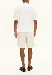 White short-sleeve button-up shirt with a textured fabric, paired with light beige shorts featuring two back pockets. Brown slip-on shoes.