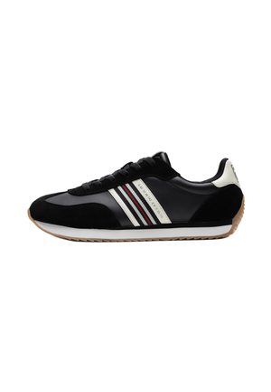 Sneaker bassa nera con dettaglio laterale a righe bianche e rosse, accento bianco sul tallone, suola in gomma e lacci neri su sfondo bianco.