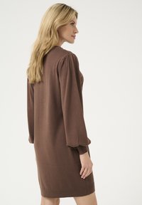 Abito lavorato a maglia marrone con maniche lunghe a palloncino, polsini a coste e orlo dritto, caratterizzato da una finitura testurizzata e un design minimalista.
