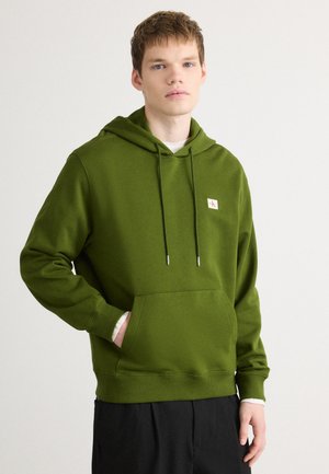 Green hoodie in soft fabric, featuring a front pocket, adjustable drawstrings, and a logo patch on the chest. Casual design, relaxed fit.