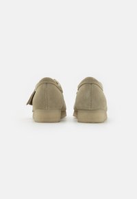 Mocassini in suede beige chiaro con punta rotonda e tacco basso, dotati di una cucitura e un piccolo dettaglio con nappina sulla parte superiore.