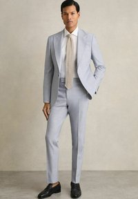 Costum gri deschis, croit pe măsură, cu un croi slim, asociat cu o cămașă albă și o cravată texturată bej. Pantofii loafers negri completează ținuta.