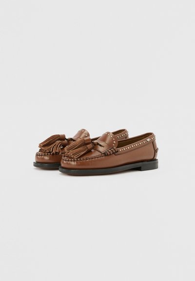 Braune Leder Slipper mit Quasten, dekorativen Nietenakzenten und einem gestickten Mokassin-Design. Flache schwarze Sohle und runde Form.