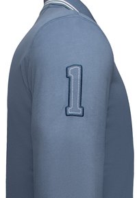 Modrý svetr s kulatým výstřihem, s vyšitým číslem "1" v světle modré a tmavě modré barvě na levém rameni.