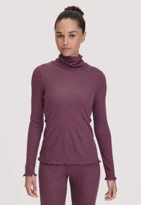 Langsleeve turtleneck top in donkerplum ribbelstof met golfvormige zoom en mouwranden, gedragen met bijpassende onderkleding, wat een samenhangende look creëert.
