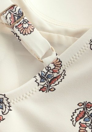 Blumenmusterstoff in Creme mit Akzenten in Blau und Rot. Verfügt über einen verstellbaren Gurt aus goldfarbenem Metall und eine strukturierte Nahtdetail.