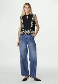 Svart ermeløs topp med blomsterbroderi og volangkant, kombinert med høy midje, løstsittende blå denimjeans og svarte spisse hæler.