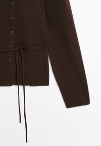 Cardigan lavorato a maglia marrone con chiusura a bottoni, coulisse regolabile in vita e maniche lunghe. I bottoni sono scuri e rotondi.