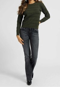 Suéter de punto verde oliva con patrón texturizado horizontal, combinado con jeans de pierna recta en gris oscuro. Botines negros de tacón completan el conjunto.