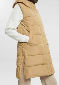 Gilet senza maniche beige imbottito con cappuccio, design trapuntato, tasche laterali, zip laterali e una superficie esterna liscia.