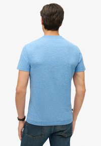 Camiseta de manga corta y cuello redondo en tela azul claro jaspeada. Diseño simple sin patrones o acentos visibles. Apta para uso casual.