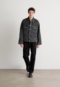 Sort denimjakke med to brystlommer, sølvhardware og en afslappet pasform, parret med sorte cargo-bukser og sorte sko.