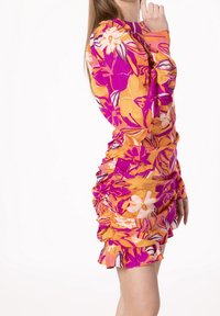 Robe ajustée à fleurs roses et orange avec des manches longues, des détails froncés et un ourlet volanté, faite d'un tissu léger.