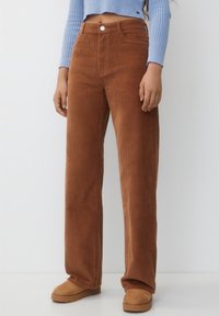 Bruna kordfløyelsvida byxor med framträdande ribbor, hög midja, framfickor och en enda framknapp. Kombinerat med en ljusblå långärmad topp.