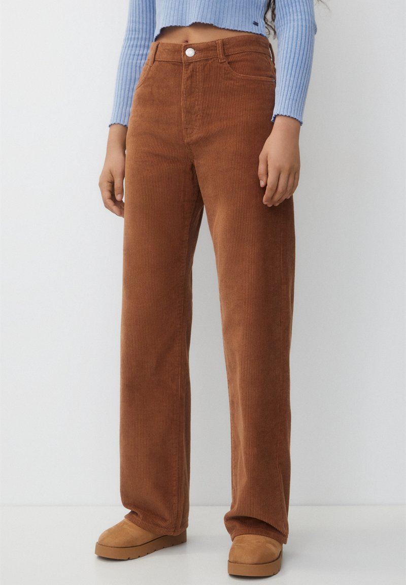 Bruna kordfløyelsvida byxor med framträdande ribbor, hög midja, framfickor och en enda framknapp. Kombinerat med en ljusblå långärmad topp.