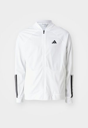 Veste blanche zippée avec un col haut, accents noirs à trois bandes sur les manches, et un petit logo noir sur la poitrine. Texture de tissu lisse.