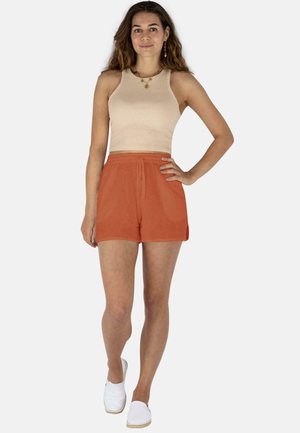 Hellbeige geripptes Cropped-Top kombiniert mit orangen Shorts, die einen elastischen Bund haben, und das Model trägt weiße Slipper.