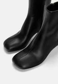 Bottines en cuir noir avec une texture lisse, un design angulaire, un bout rond et un détail de fermeture éclair sur le côté.
