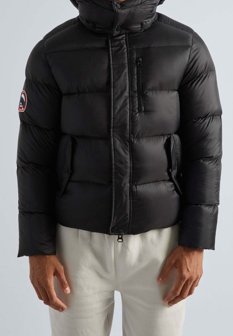 Veste matelassée noire avec un col haut, une poche poitrine zippée et des poches latérales ; caractérisée par une texture matelassée et des poignets élastiques.