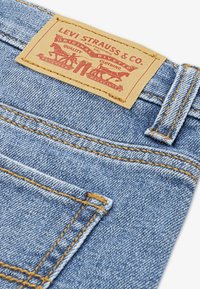 Τζιν παντελόνια από ανοιχτό μπλε τζιν με υφή στην επιφάνεια, με καφέ δερμάτινη ετικέτα με κόκκινη εκτύπωση, κίτρινη ραφή και λεπτομέρειες στην πίσω τσέπη.