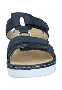 Mörkblå sandal med breda remmar, en cirkulär metallackcent och en vadderad beige innersula. Har en vit, texturerad sula för bra grepp.