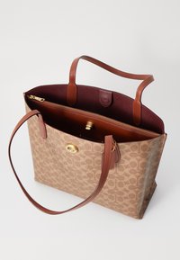 Brown patterned tote bag with leather handles, open top, and interior zip pocket. Features gold-tone hardware and a burgundy lining.