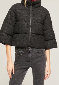 Mustat, teksturoidut, lyhyet pufftakki, jossa on kolmen neljänneksen hihat, yhdistetty korkeavyötäröisiin mustiin farkkuihin, joissa on niitattu etutaskut.