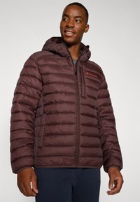 Ciemno bordowa kurtka puchowa z kapturem, z pikowanym wzorem, widocznym zamkiem błyskawicznym i kieszeniami, logo na piersi oraz elastycznymi mankietami.