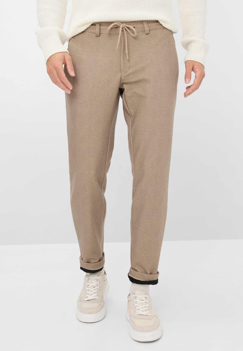 Pantalons à carreaux beige avec une taille à cordon, jambes fuselées et ourlets retroussés, associés à des baskets blanches. Texture de tissu douce.