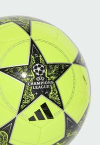 Žlutý fotbalový míč s černými detaily, se vzorem hvězdy, logem UEFA Champions League a značkou Adidas. Velikost 5. Hladká textura.