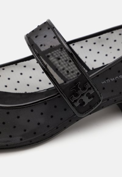 Schwarzer Schuh mit Punkten, der ein strukturiertes Mesh-Obermaterial aufweist, mit einem breiten Riemen und einem dekorativen schwarzen Logo-Akzent auf dem Riemen.